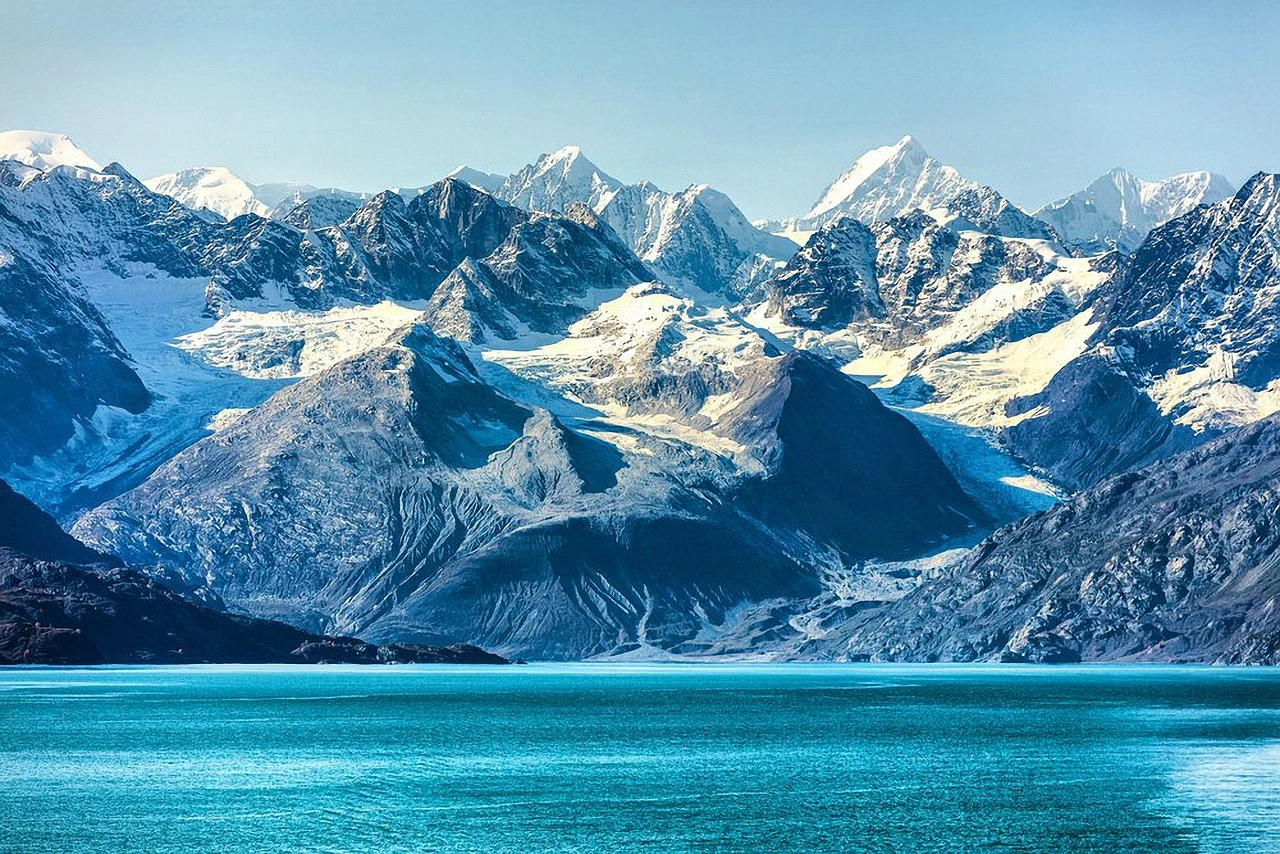 im Hintergrund schneebdeckte Berge, im Vordergrund eisblaues Meer