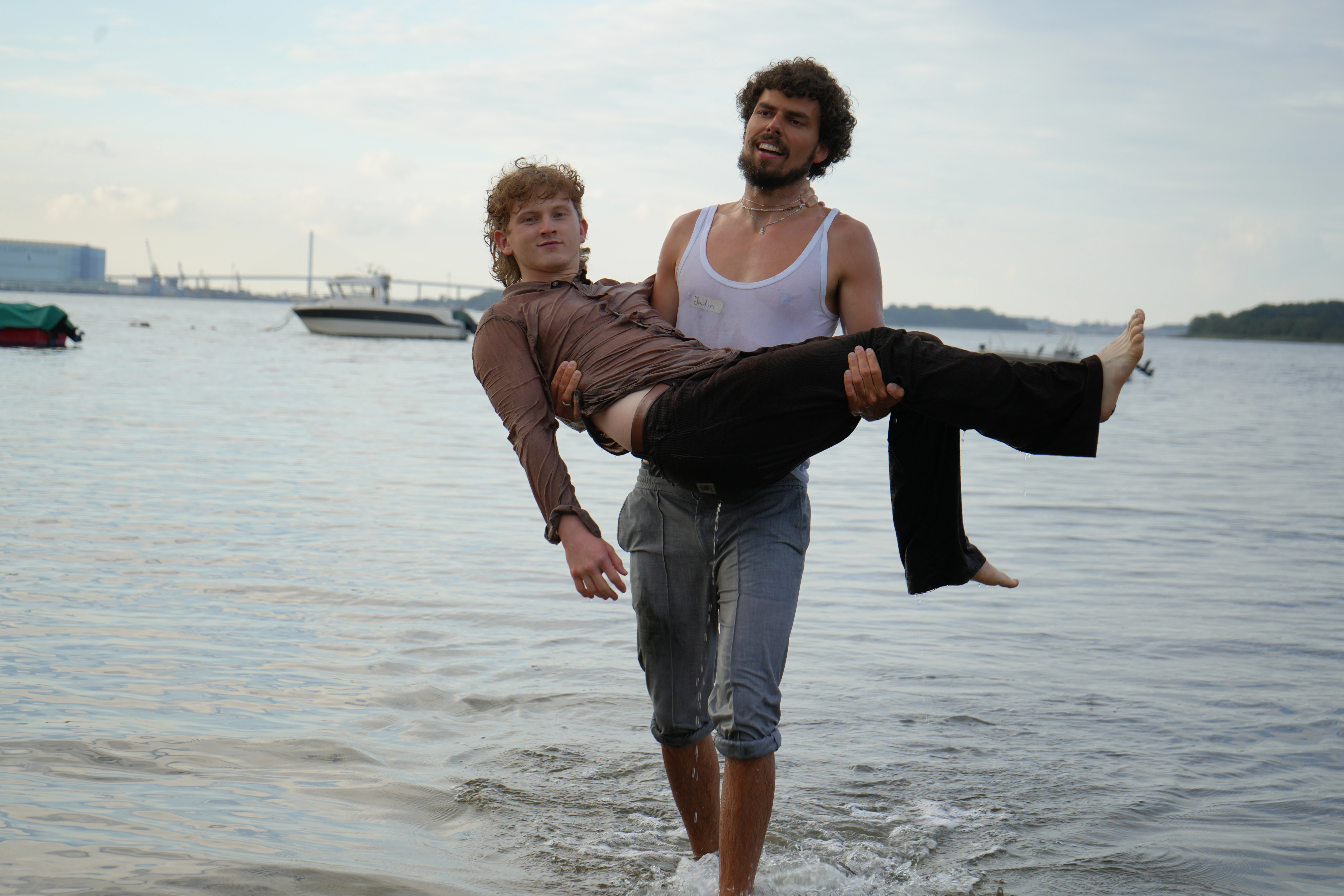 Justin steht bis zu den Knöcheln im Wasser und trägt Marvin wie eine Prinzessin auf dem Arm. Die beiden sind offensichtlich sehr nass vom Toben in der Ostsee.