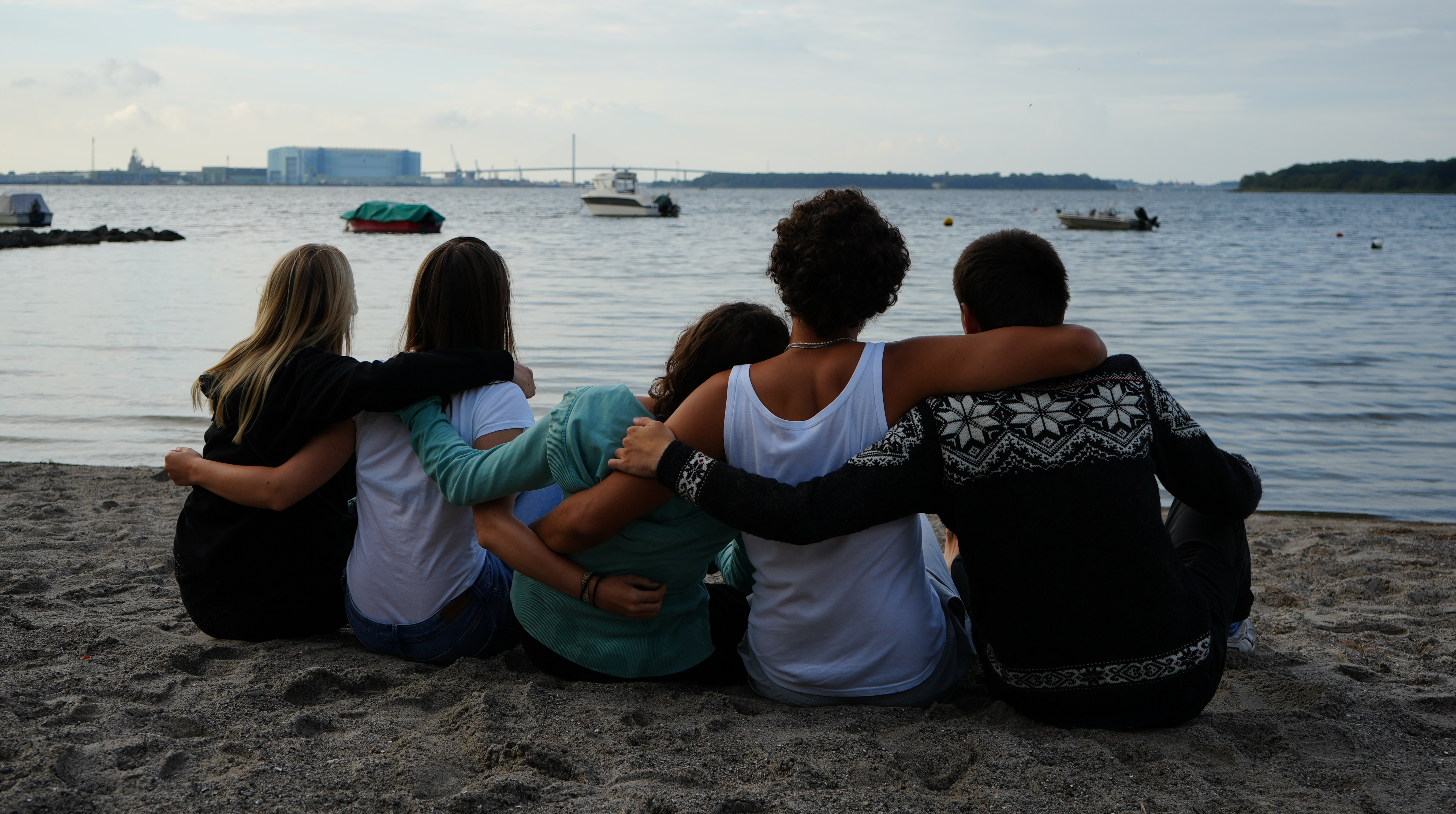 Eine Gruppe von fünf Menschen sitzt mit dem Rücken zum Bild am Strand und blickt über die Ostsee.