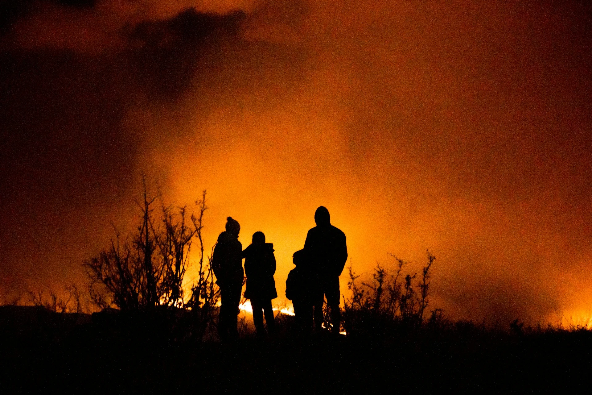 Vier Menschen stehen bei Nacht vor einer großen brennenden Fläche