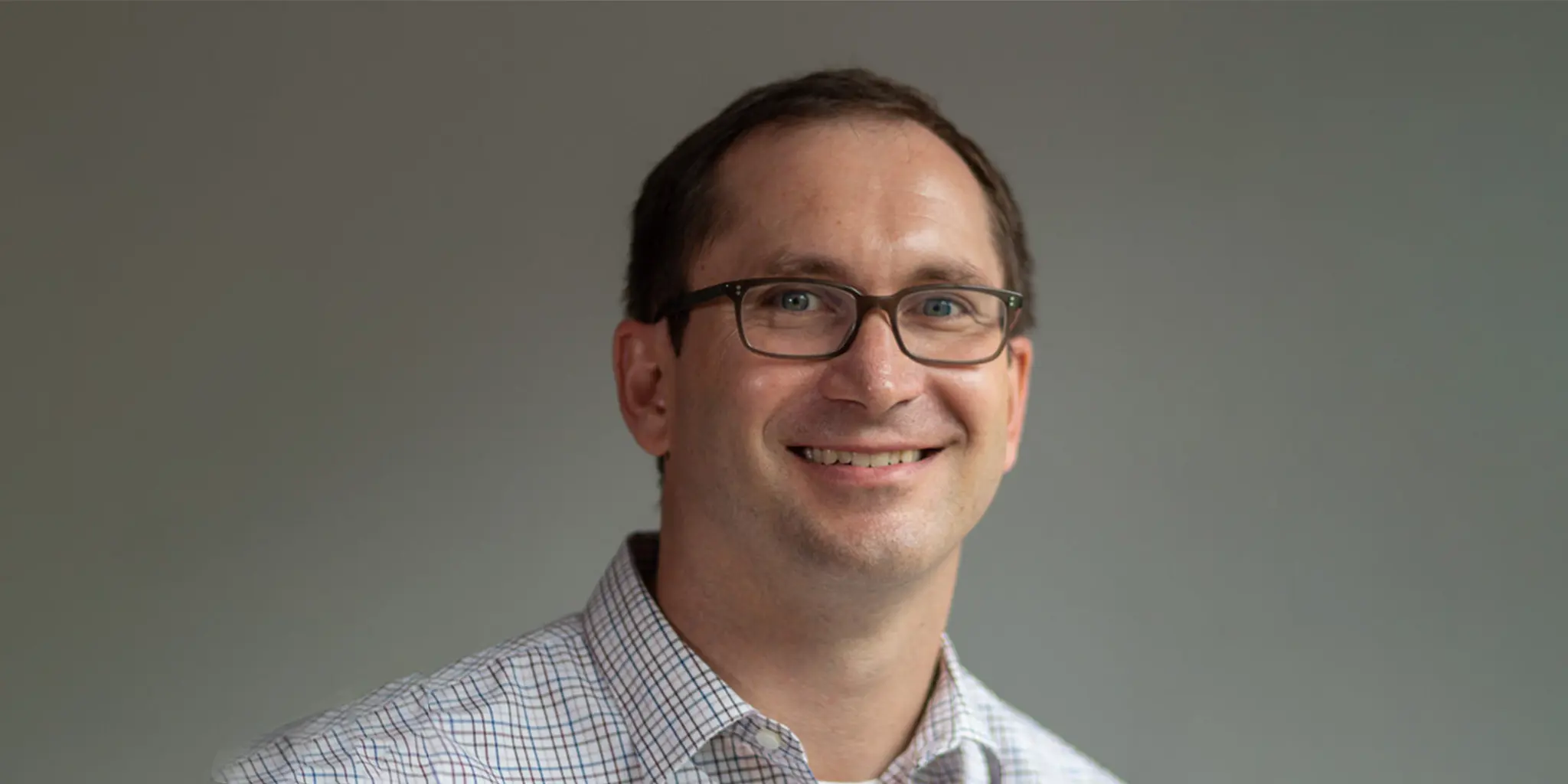 A man with glasses smiles at the camera