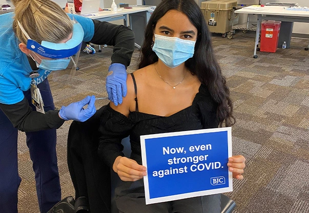 Nataly in a black shirt getting the vaccination from a person in scrubs