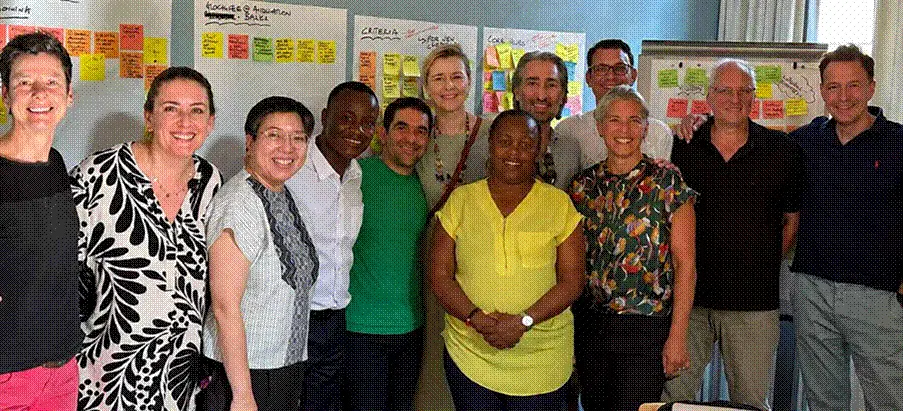 Title: Glocalization kickoff - Description: Board members and country team representatives smiling together in front of a wall of workshop notes at the Glocalization kickoff.